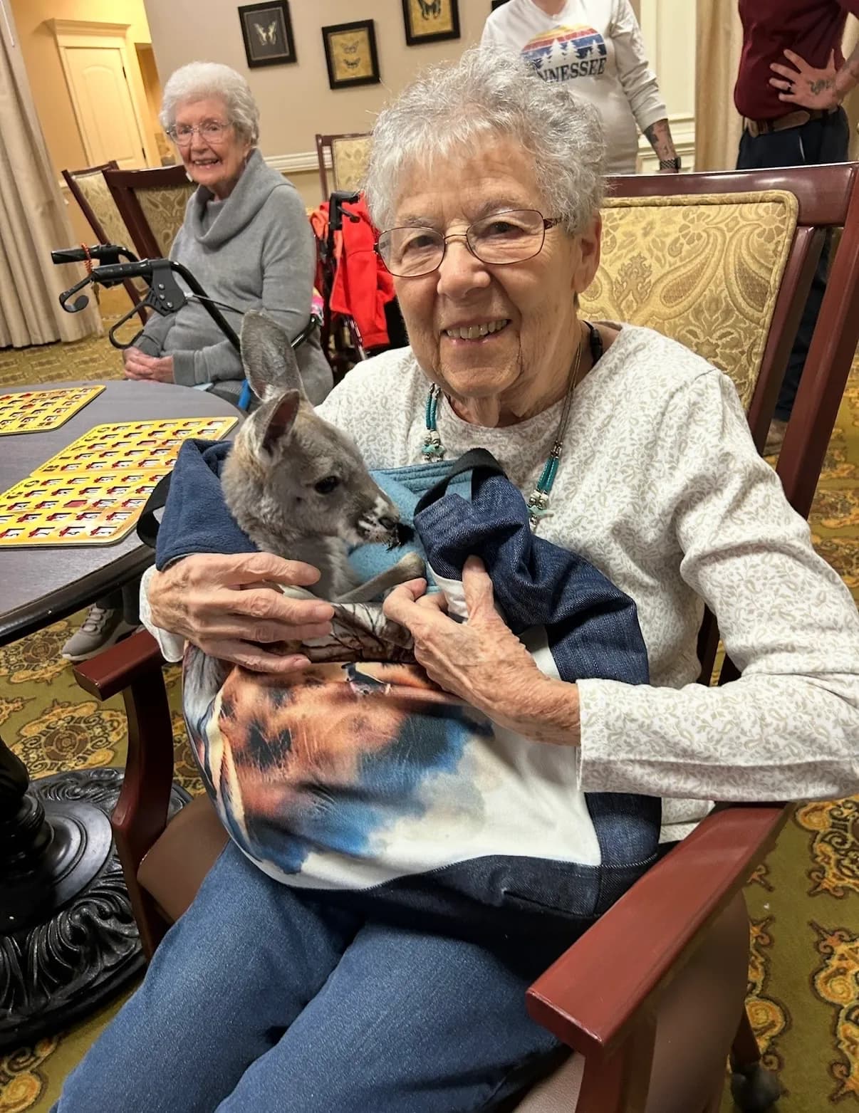 Elderly woman beaming while holding Sophie the kangaroo in her lap